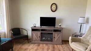 A living room with a wooden entertainment center, a television, a fireplace, a lamp, and a chair.