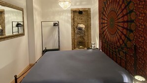 A bedroom with a bed, a stone wall, a tapestry, and a chandelier. - Elegant and Cozy Appartement with Wifi and Garden in Heart of Charming Telavi (Telavi)