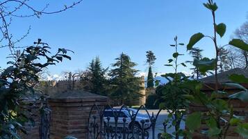 A gated entrance with a brick wall and wrought iron gate, leading to a parking area with a car.