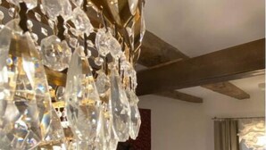 A room with a chandelier made of clear crystals, a patterned tapestry on the wall, a blue sofa with cushions, and a floor lamp. - Elegant and Cozy Appartement with Wifi and Garden in Heart of Charming Telavi (Telavi)