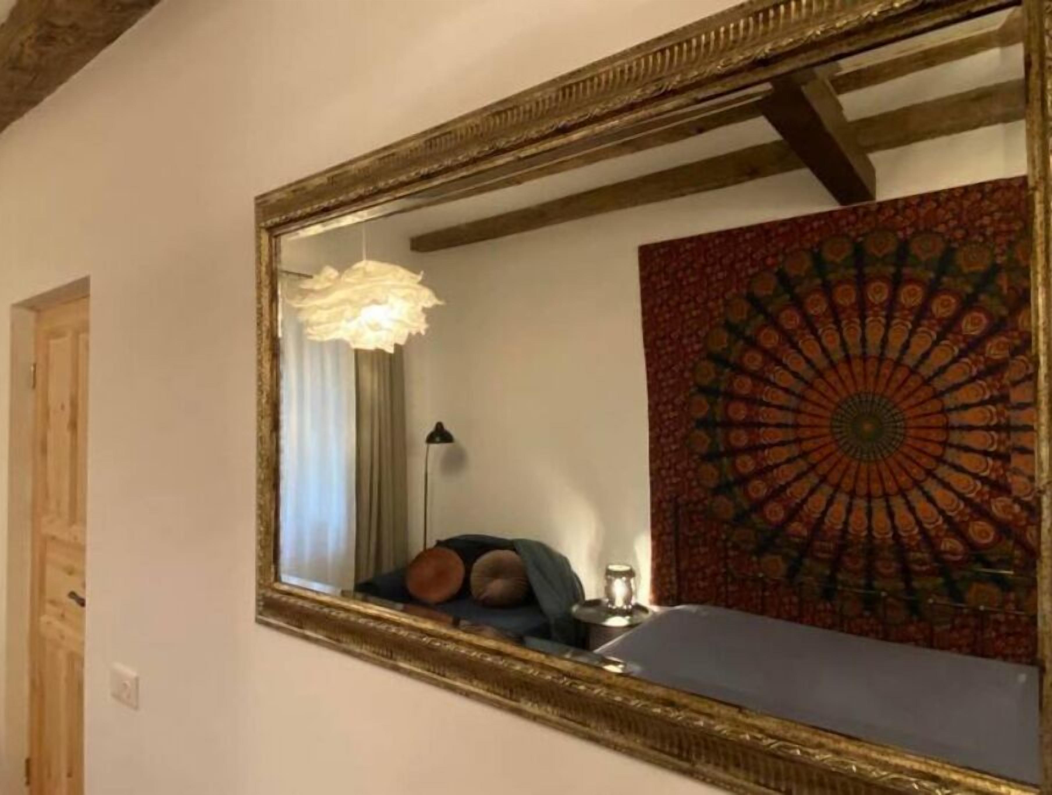 Quarto com um espelho grande, tapeçaria estampada, cama com almofadas, abajur e ventilador de teto.