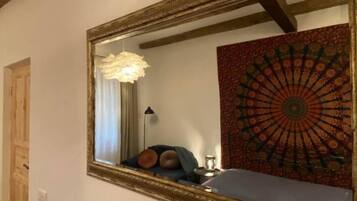 Quarto com um espelho grande, tapeçaria estampada, cama com almofadas, abajur e ventilador de teto.