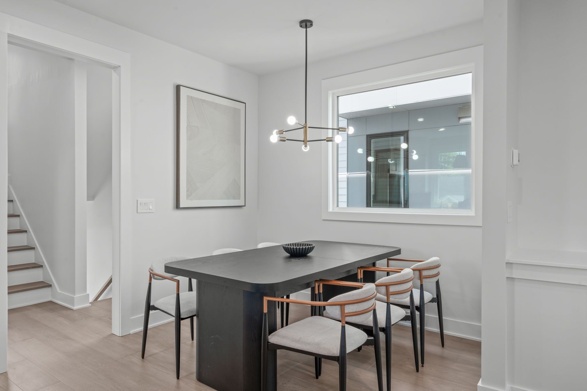 Un comedor moderno con una mesa de madera oscura, seis sillas, una lámpara colgante y un ventanal grande.