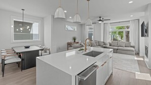 A modern kitchen with a central island, pendant lights, and a dining area with chairs.