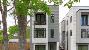 A modern multi-story residential building with a flat roof, large windows, and a wooden fence in the foreground.