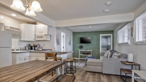 A modern kitchen with white cabinets, a wooden dining table, and a bar area. - Seashore Condo Hotel Two Bedroom Suite, Spacious Fire Island Escape, Near Ferry - With Bay Views and Steps from the Beach. (Ocean Bay Park)