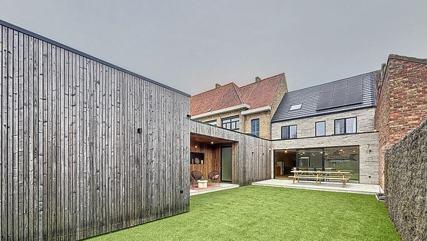 A modern house with a wooden exterior, a well-maintained lawn, and a patio area with outdoor seating. - Maison Martha - Oostduinkerke (Koksijde)