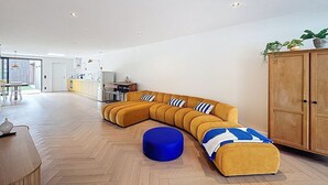 A modern living room with a large L-shaped sectional sofa, a blue ottoman, and a wooden cabinet. - Maison Martha - Oostduinkerke (Koksijde)