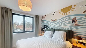 A hotel room with a large bed, a window with curtains, a wall mural, and a bedside table with a lamp. - Maison Martha - Oostduinkerke (Koksijde)