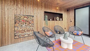 A modern outdoor seating area with wooden panel walls, a stone wall with wood logs, and black wicker chairs with colorful cushions. - Maison Martha - Oostduinkerke (Koksijde)