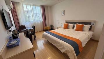 A hotel room with a bed, desk, chair, and a television.