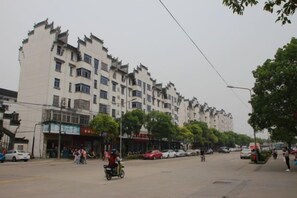 A street with a multi-story building, parked cars, and a few people. - Shanghai Jinxiang Hotel (Zhujiajiao Ancient Town) (Shanghai)