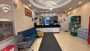A hotel lobby with a reception desk, a blue sofa, a small round table, and a water dispenser.