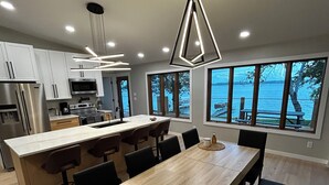A modern kitchen with a central island, stainless steel appliances, and large windows offering a view of the water.