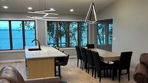 A modern kitchen with a central island, dining area with chairs, and large windows offering a view of the water.