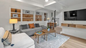 A modern living room with a sofa, coffee table, and TV. There are shelves with decorative items and a lamp. - Stunning Neighborhood Home Walkable to Downtown Mill Valley (Mill Valley)