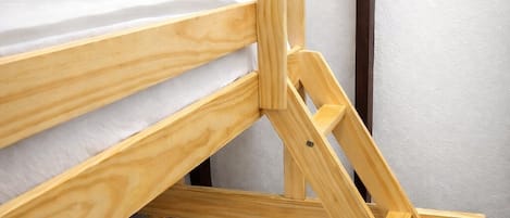 A bunk bed with a wooden frame and a mattress with a gray and white patterned pillow.
