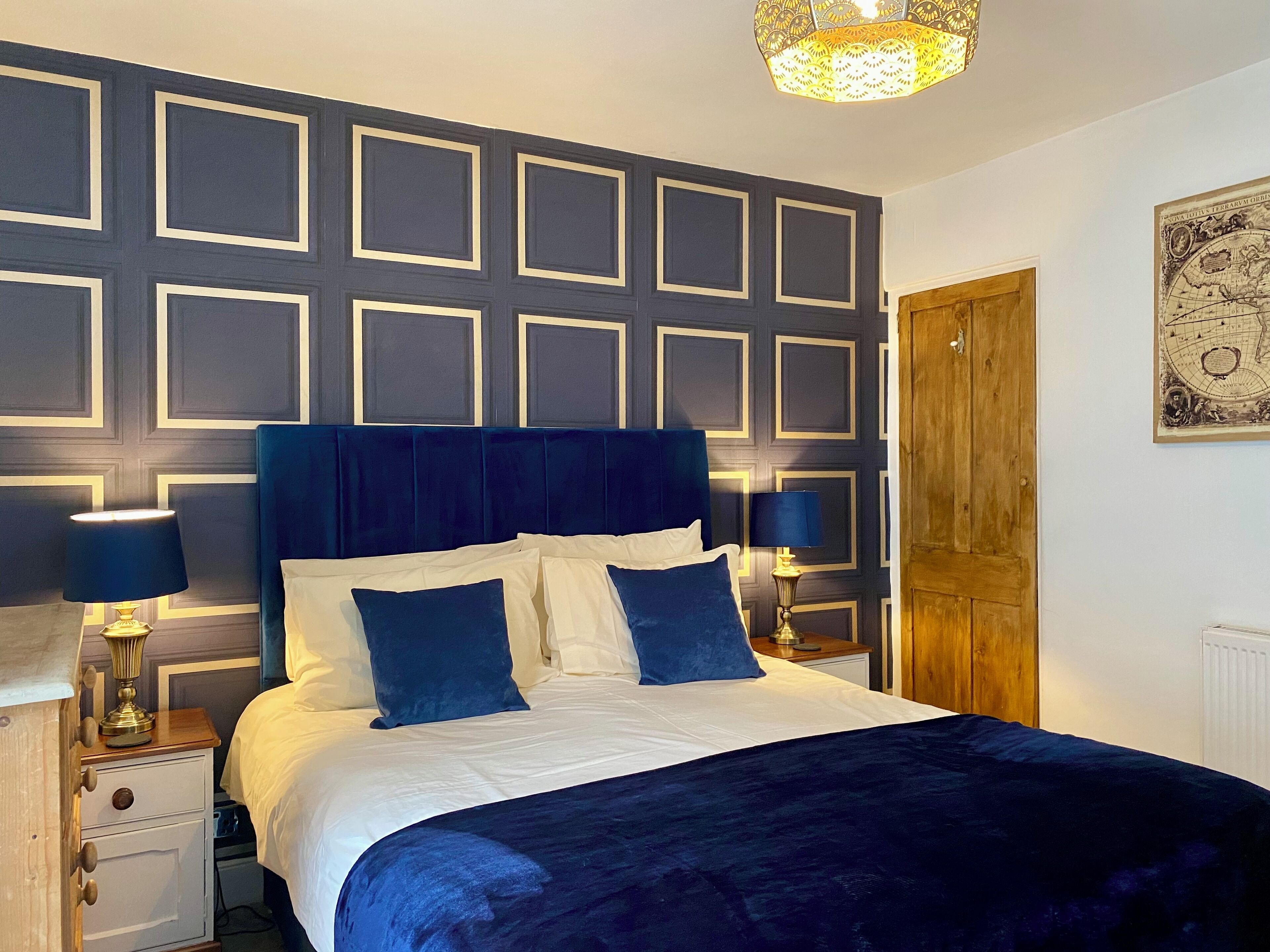 Une chambre à coucher avec un grand lit, deux tables de chevet avec des lampes, une porte en bois et un mur orné d’un motif géométrique.