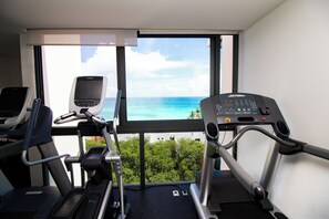 Une salle de sport équipée de tapis de course et d’un vélo d’appartement, une grande fenêtre donnant sur l’océan et un panneau de commande sur le vélo.