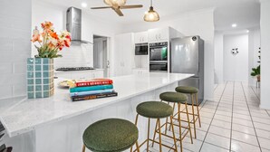 Una cocina moderna con armarios blancos, una isla grande con taburetes, un ventilador de techo y un florero con flores.