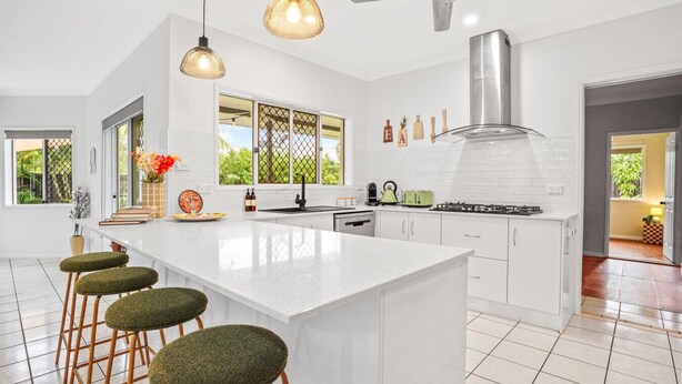 Cocina moderna con una isla grande, taburetes de bar, ventilador de techo y vistas al exterior.