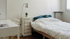 Une chambre à coucher avec un lit en bois, un bureau blanc, une lampe, un radiateur et un tableau encadré au mur.
