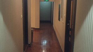 Un couloir étroit, doté d’un plancher en bois et de murs de couleur beige, qui mène à une porte sur laquelle est apposée une enseigne verte indiquant la sortie.