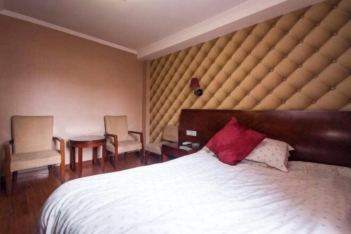 A hotel room with a large bed, two armchairs, a small round table, and a tufted headboard.