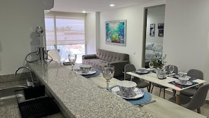 A modern kitchen with granite countertops, a dining area with a table set for four, and a living area with a sofa and a painting on the wall. - OCEAN DRIVE, Apartamento frente al mar (Cartagena)