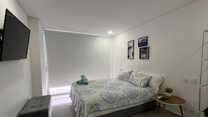A modern bedroom with a bed, a small table, a bench, and a TV mounted on the wall. - OCEAN DRIVE, Apartamento frente al mar (Cartagena)