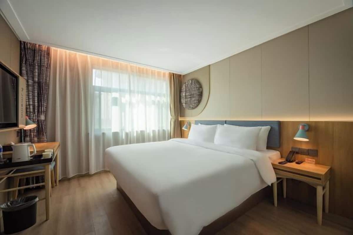 Une chambre d’hôtel avec un grand lit, un bureau avec une lampe, une télévision et une horloge fixée au mur.