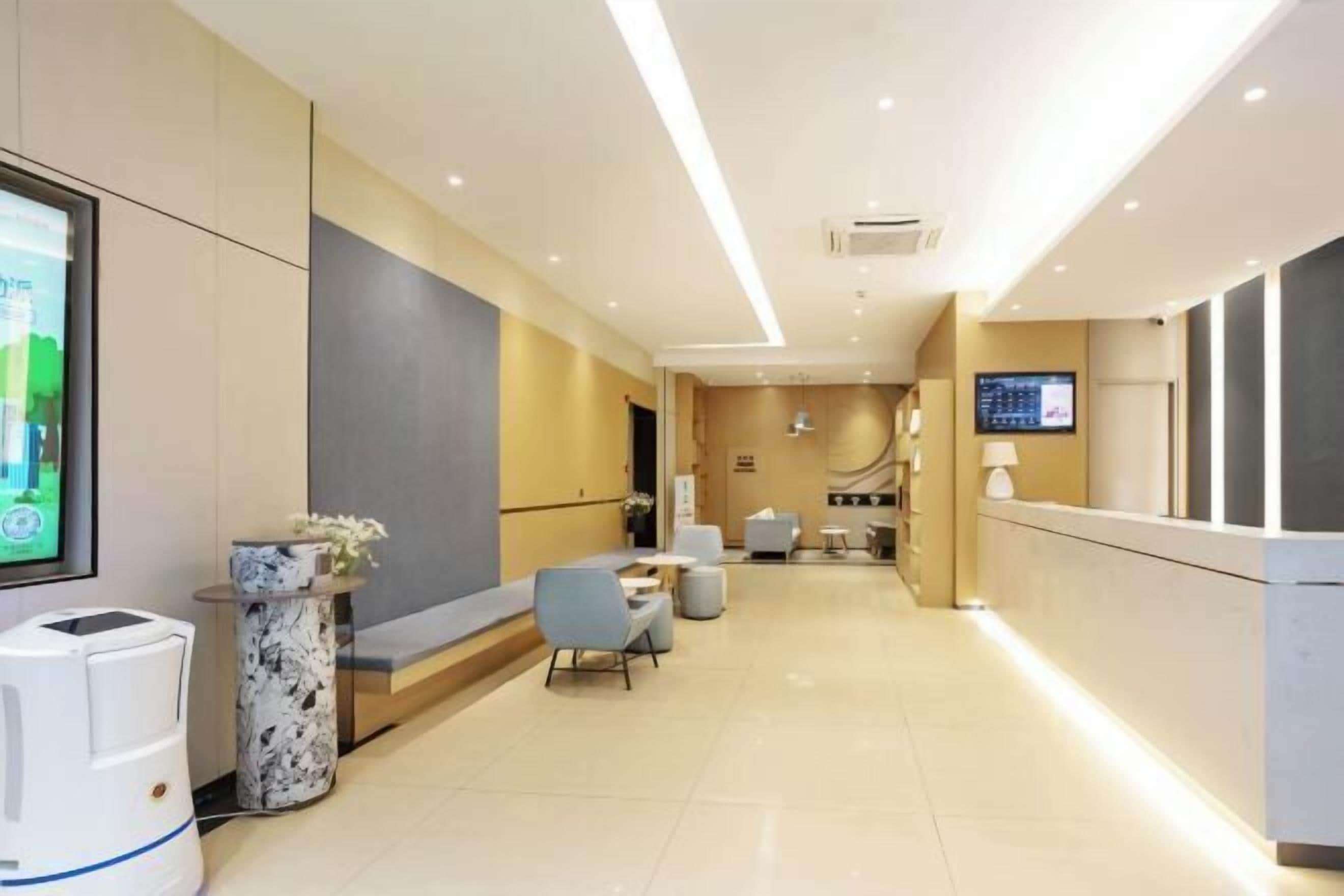 A modern hotel lobby with a reception desk, seating area, and a large screen.