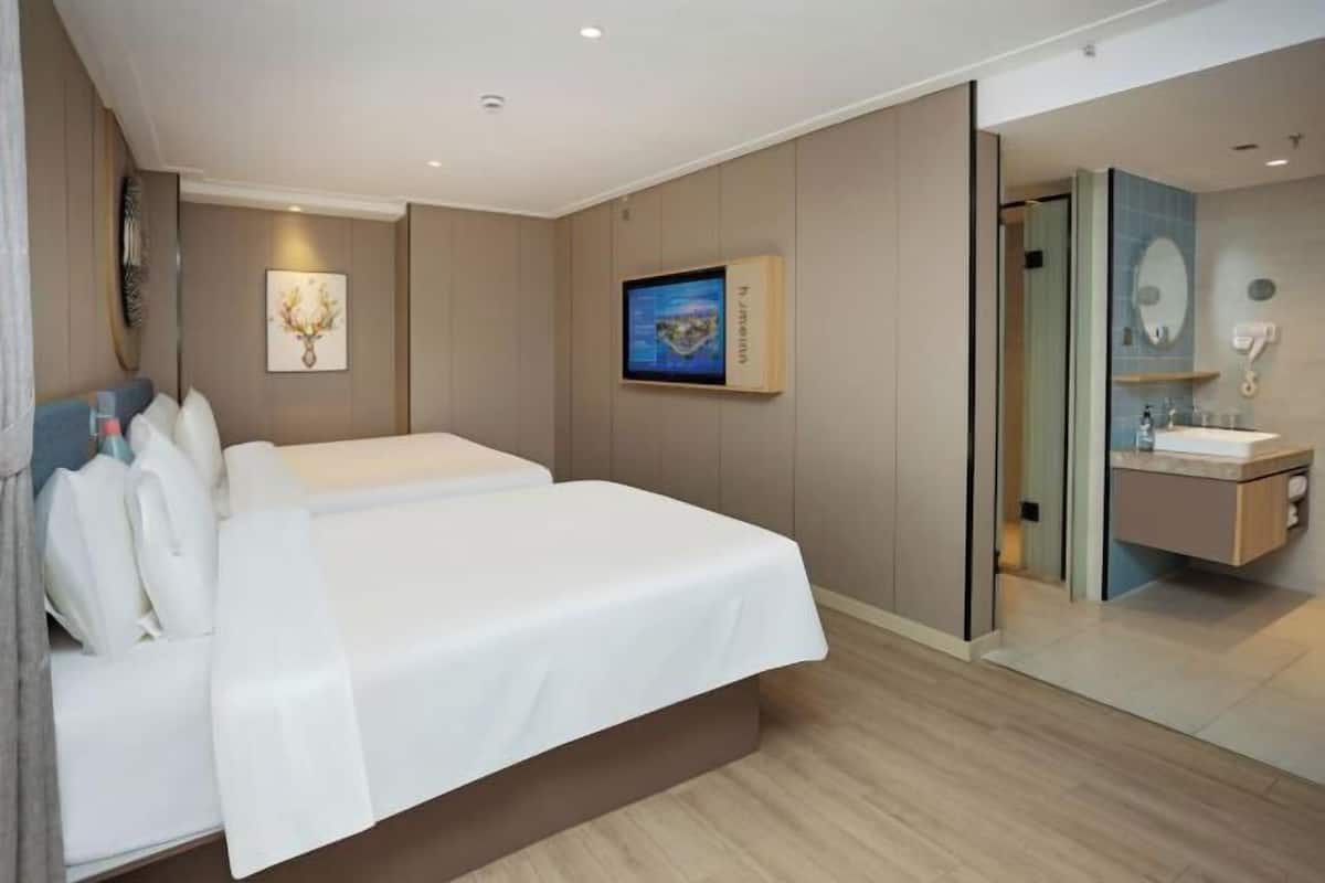 Une chambre d’hôtel comprenant un lit, une télévision, une salle de bain avec un miroir et un lavabo, ainsi qu’une œuvre d’art accrochée au mur.