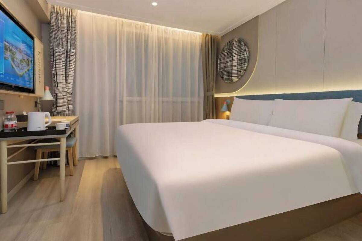 Une chambre d’hôtel avec un lit, un bureau et une chaise, une télévision et des rideaux.