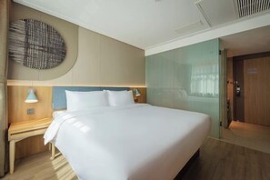 Habitación de hotel con una cama grande, una mesita de noche con lámpara, una obra de arte colgada en la pared y una puerta a la derecha.