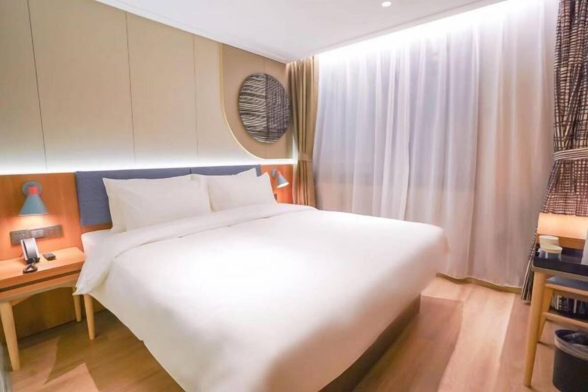 Une chambre d’hôtel avec un lit, des tables de chevet, une lampe, un tableau décoratif et un rideau.