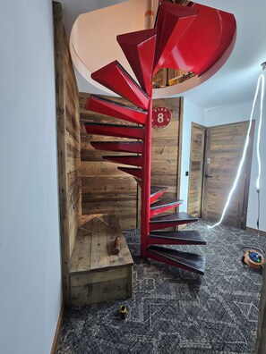 A spiral staircase with red steps and a wooden wall.