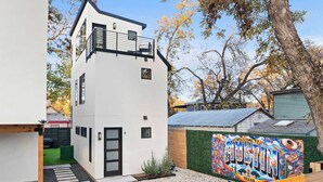 A modern two-story building with a balcony, a small garden area, and a colorful mural on the side.