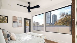 A modern bedroom with a large bed, a ceiling fan, and a city view through large windows.