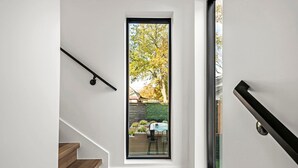 A modern interior with a wooden staircase, a glass door leading to an outdoor area with a view of trees and a garden.