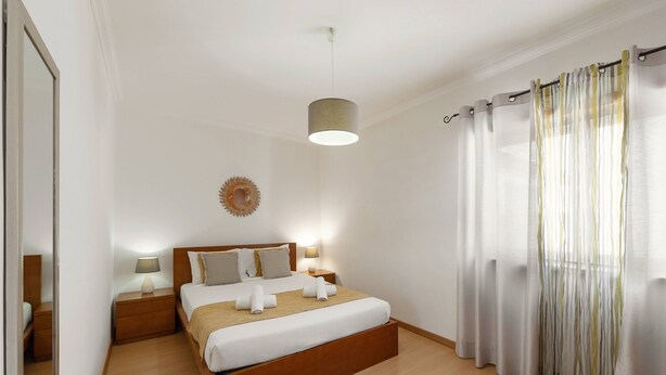 Une chambre à coucher bien rangée, avec un lit en bois, des lampes de chevet, une horloge murale et des rideaux légers.