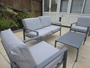 Une terrasse extérieure avec une table en métal gris et deux chaises grises rembourrées.
