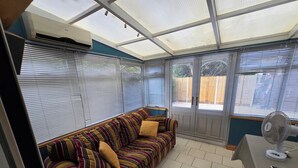 Een kamer met een gestreepte bank, een tafel met een ventilator en een raam met jaloezieën.