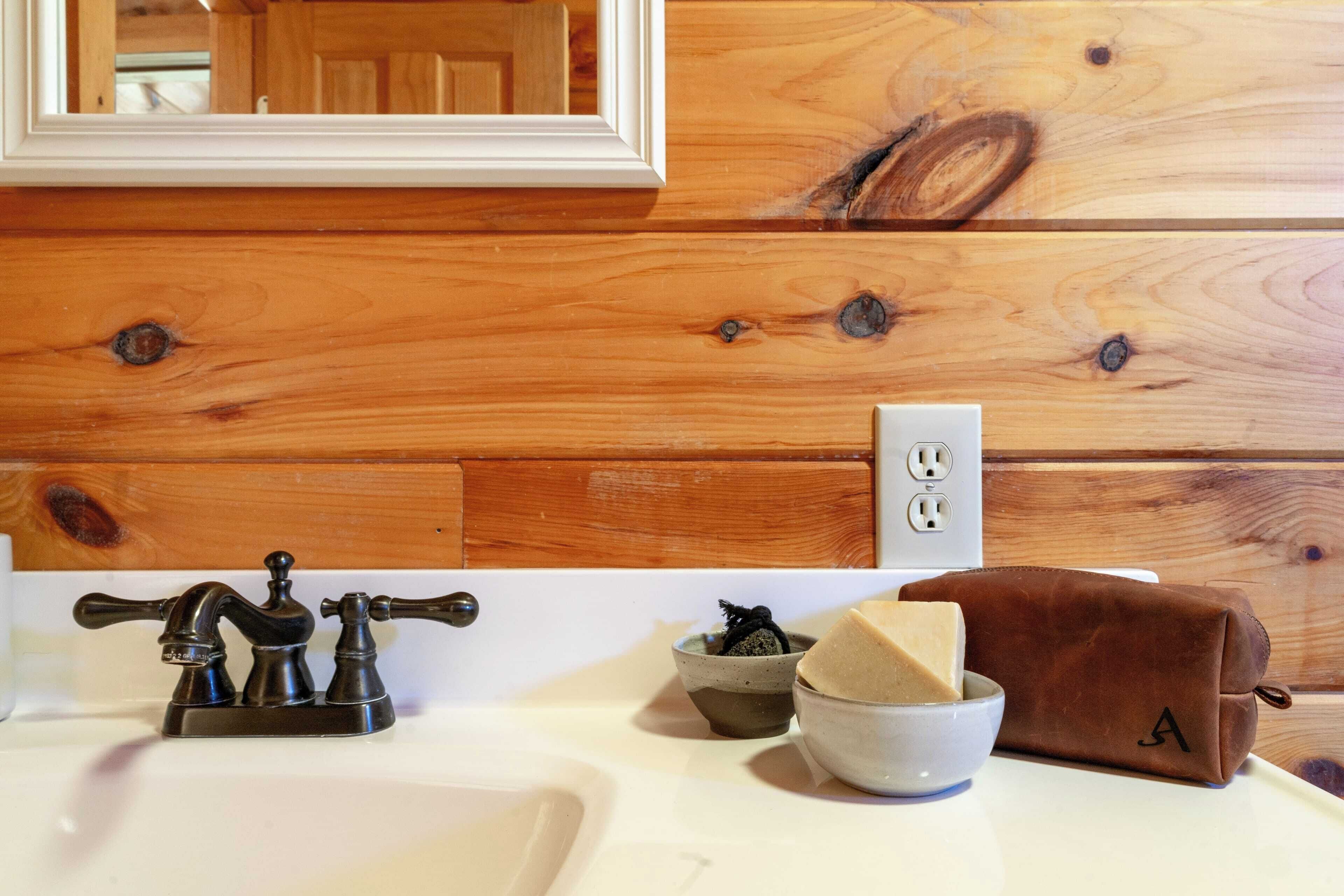 A bathroom with a wooden panel wall, a white sink, a mirror, and a brown leather bag on the counter.