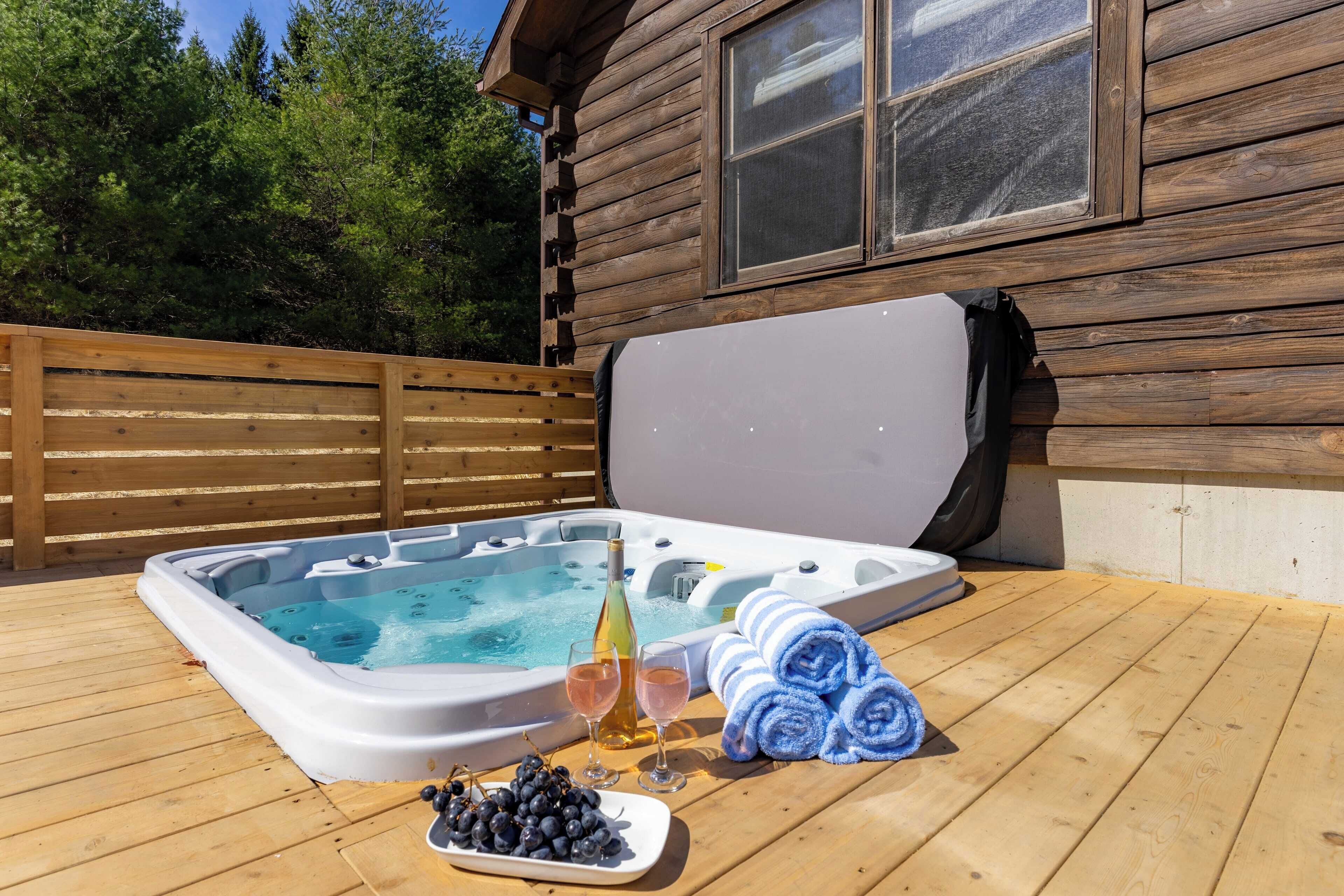 Una cabaña de madera con jacuzzi, una botella de vino, copas y toallas sobre una terraza de madera.
