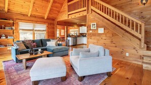 A spacious living area with a wooden staircase, a sofa set, and a kitchen in the background. - Secluded w/ Deck Views, Hot Tub, & Ping Pong Hudson in the Berks by Avantstay (East Chatham)