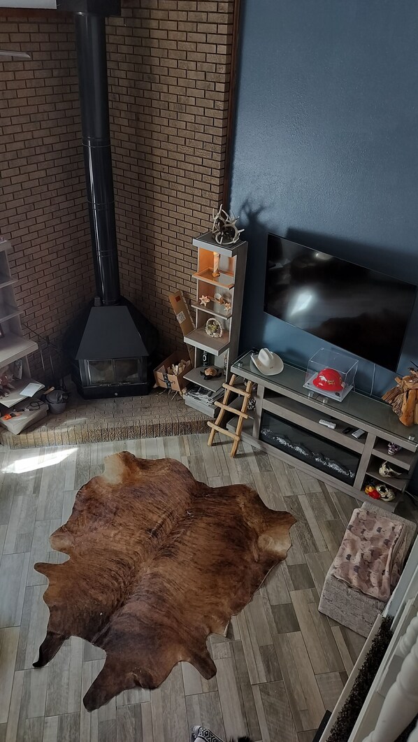 Uma sala de estar aconchegante com parede de tijolos, lareira preta, televisão e um tapete grande de couro.