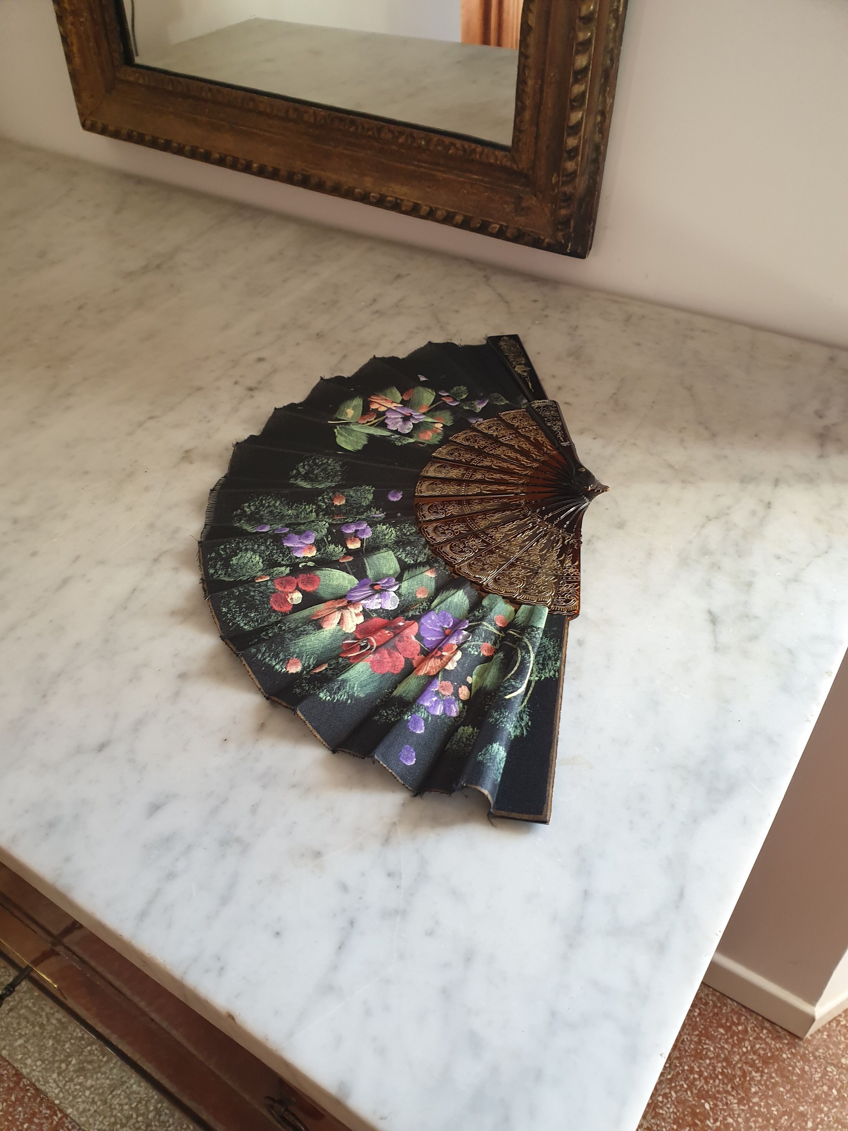Een decoratieve waaier met bloemenmotieven op een marmeren oppervlak.