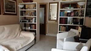 A living room with a sofa, a chair, a bookshelf, a radiator, and a clock on the wall. - DUETERRE ROOM & HOST (Amelia)