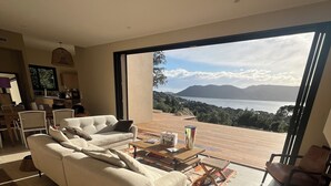 Een moderne woonkamer met een grote bank, een salontafel en uitzicht op zee door grote ramen.